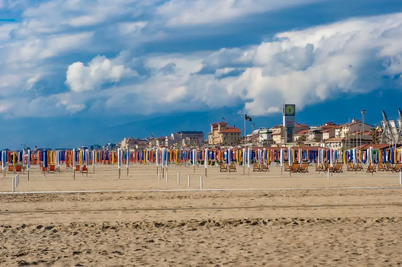 Scenic view of vibrant beach umbrellas and chairs on an Italian coast under dramatic clouds.
