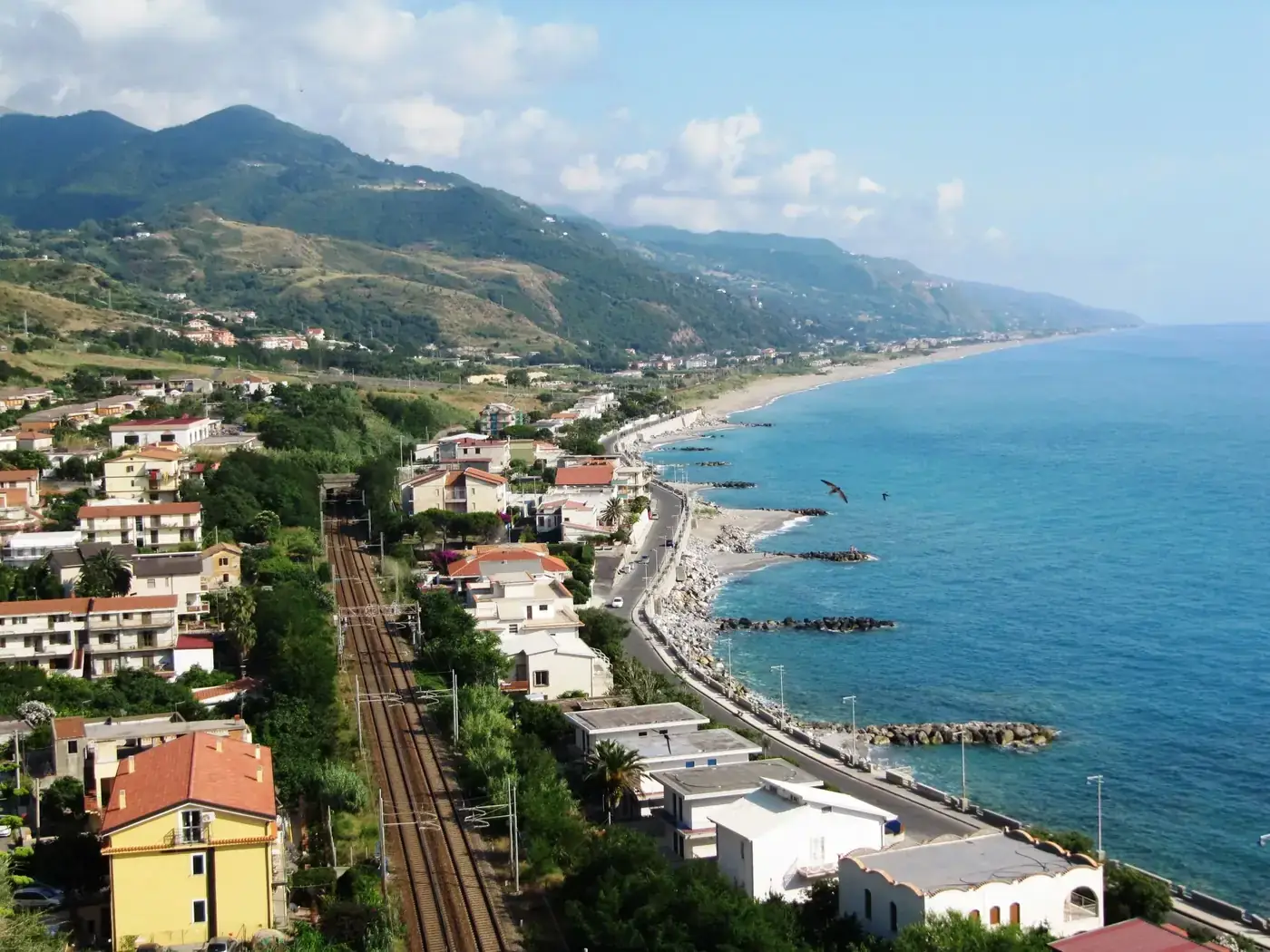 A stunning view of Calabria's coastline with railway tracks by the sea on a sunny day.
