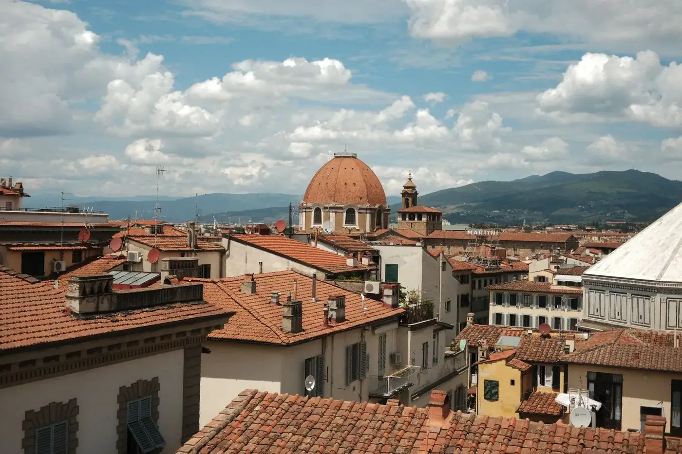 A picturesque view of Florence rooftops with a dome under a bright, cloudy sky.