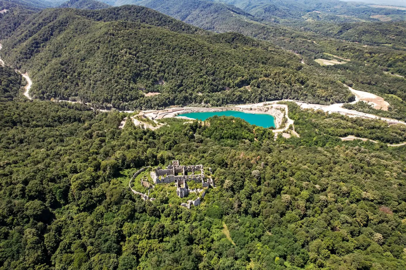 A spectacular aerial view of ancient ruins surrounded by lush greenery and a turquoise lake in Orahovica, Croatia.