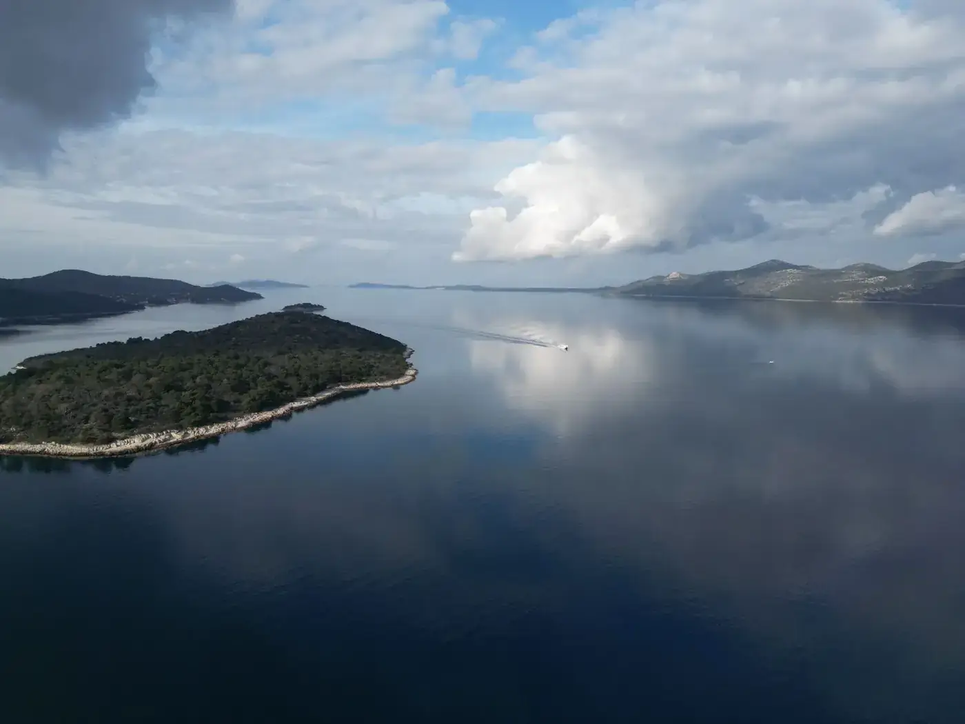 Serene aerial shot of Mali Iž island reflecting on the Adriatic Sea with a cloudy sky.